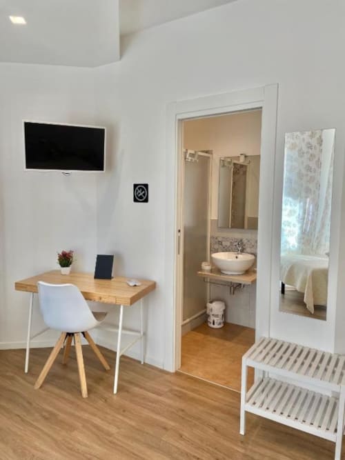 Modern hotel room at Catalogna10 in Alghero with desk, white chair, flat-screen TV, and ensuite bathroom