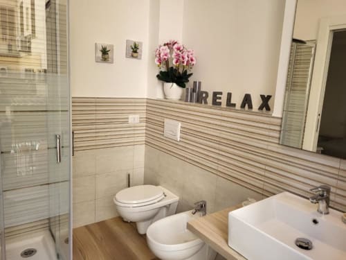 Modern bathroom at Catalogna10 Rooms in Alghero with striped tile walls, white fixtures, pink flowers, and 'RELAX' wall text