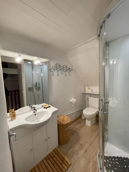 Salle de bain moderne de l'appartement La Brigantine à Loc'Maria, Belle Île en Mer, avec lavabo blanc, toilettes, douche et sol en bois