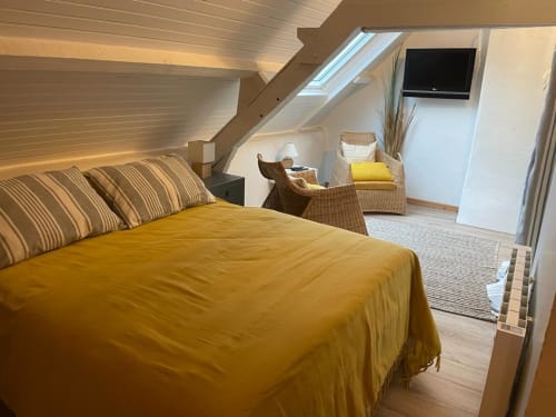 Chambre de l'appartement La Brigantine avec literie moutarde, puits de lumière, coin détente en rotin et télévision écran plat, Belle Île en Mer