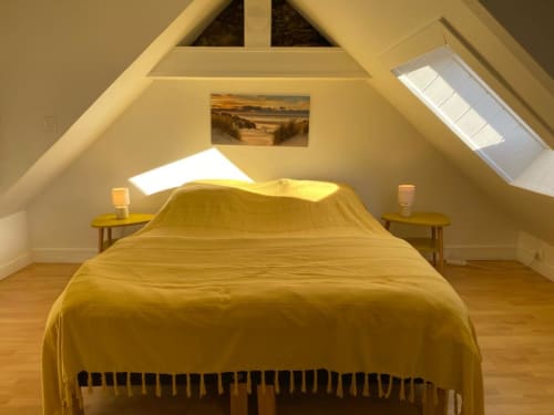 Chambre sous les combles ensoleillée avec literie jaune, lucanes, tables de nuit en bois et art côtier aux Galets