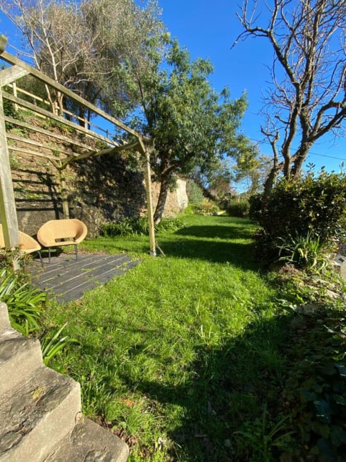 Vue paisible du jardin du gîte Locmaria avec pelouse verdoyante, pergola, et arbres matures sous ciel dégagé