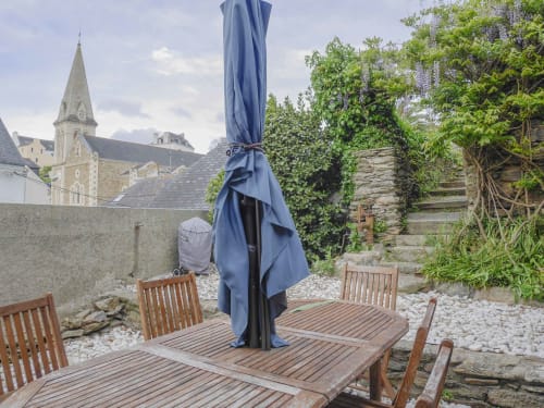 Terrasse de jardin avec terrasse bois, parasol bleu et chaises avec vue sur l'église de Belle-île-en-Mer et les murs en pierre à Loc'Maria
