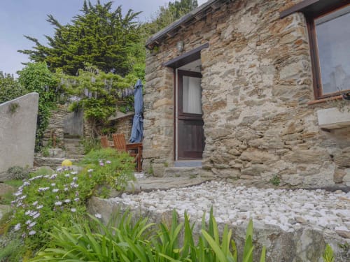Entrée du jardin de maison en pierre avec gravier blanc, plantes fleuries et mobilier en bois à Loc'Maria, Belle Île