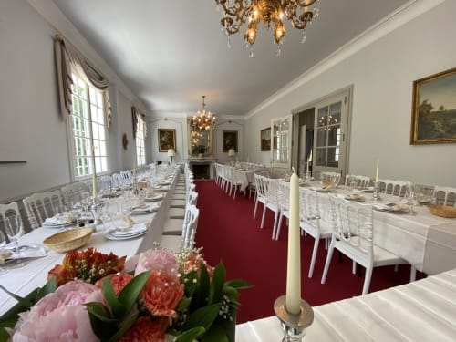 Eleganter Bankettsaal im Domaine de Bize Mirepoix mit weißen Stühlen, rosa Blüten und Kristalllüstern zur Hochzeit