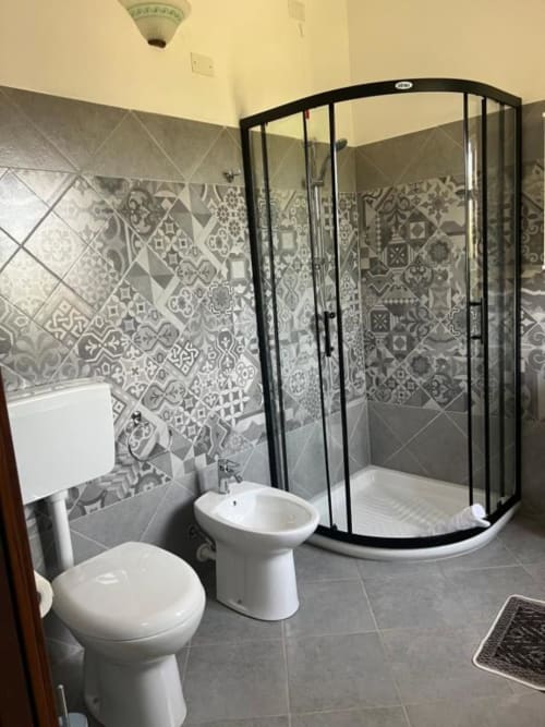Bagno moderno all'Agriturismo Su Barraccu a Loceri con doccia in vetro curvo, water, bidet e piastrelle decorate