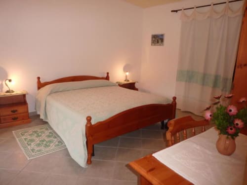Camera accogliente all'Agriturismo Su Barraccu a Loceri con letto in legno, biancheria bianca e vista sul giardino