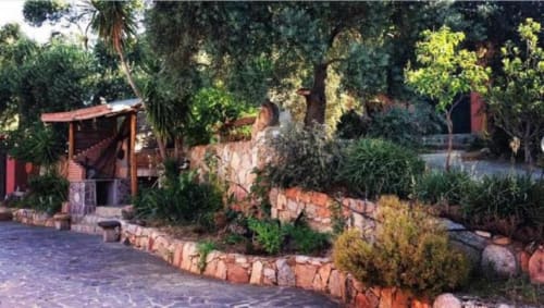 Cortile di Agriturismo Su Barraccu a Loceri con edifici rustici, sentieri in terracotta e rigogliosa vegetazione mediterranea