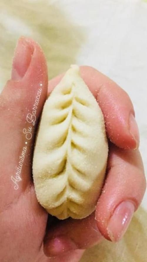 Hand holding traditional Italian bread with leaf pattern from Agriturismo Su Barraccu, Loceri