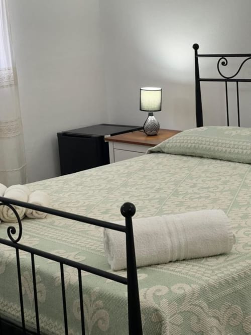 Camera moderna all'Agriturismo Su Barraccu a Loceri con letto in ferro nero, biancheria bianca, lampada comodino e giardino