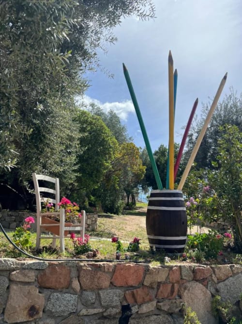 Giant colored pencils in barrel and white chair with flowers at Agriturismo Su Barraccu garden in Loceri