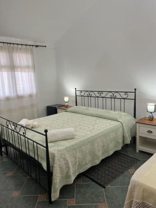 Camera luminosa con letto in ferro battuto e biancheria crema presso l'Agriturismo Su Barraccu di Loceri, Italia