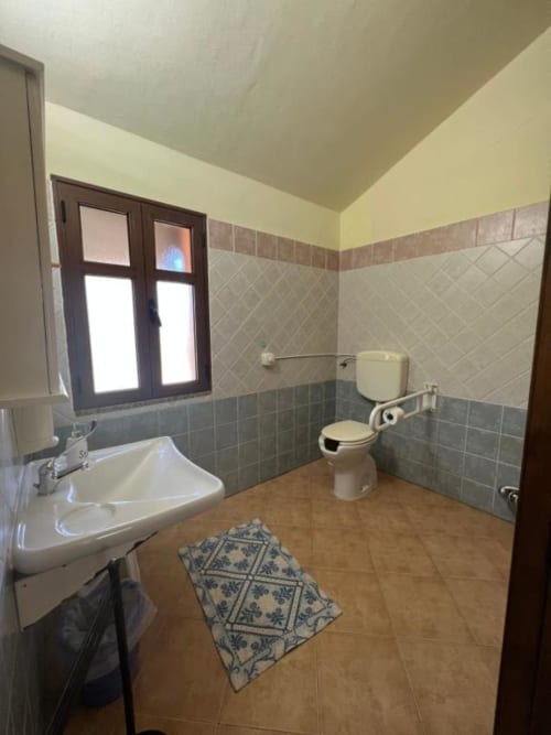 Spacious bathroom at Agriturismo Su Barraccu in Loceri with tiled walls, sink, toilet, and decorative floor mat