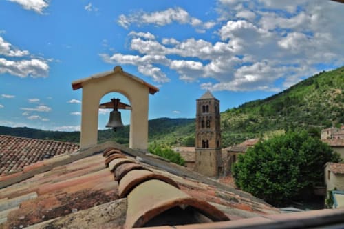 Glockenturm und Steinkapelle mit Blick auf das Dorf Moustiers-Sainte-Marie, eingebettet in grüne Hügel unter blauem Himmel