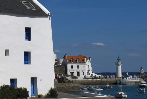 Bâtiment côtier blanc aux portes bleues dominant le port, phare visible à Loc'Maria, Belle-Île-en-Mer