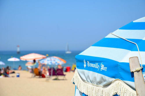 Blue and white striped beach umbrella at Hotel Le Trouville with sandy beach and sailboats in Trouville sur Mer