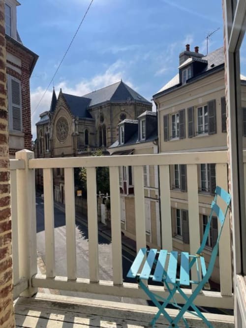 Balcony view from Hotel Le Trouville with blue deck chair overlooking historic church and French architecture in Trouville