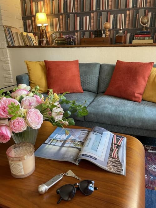 Elegant living room at Hotel Le Trouville with gray sofa, colorful pillows, bookshelf, pink flowers, and magazines on wooden