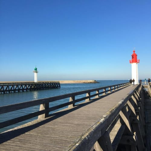 Wooden pier with red and white lighthouse at Trouville-sur-Mer, featuring clear blue sky and sandy beach