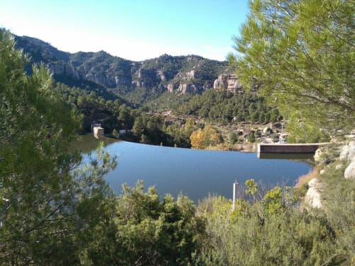Vista del lago de montaña con colinas boscosas y estructuras de piedra en Cuartel del Montsant, La Granadella