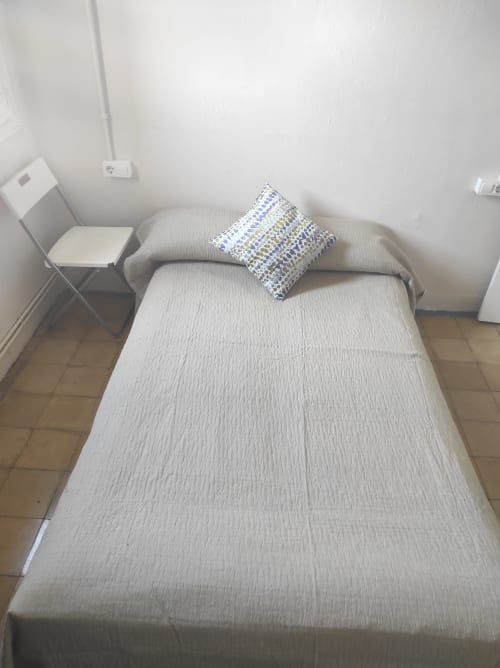 Dormitorio minimalista en Cuartel del Montsant con cama color crema, almohada azul estampada y silla blanca en apartamento La Granadella