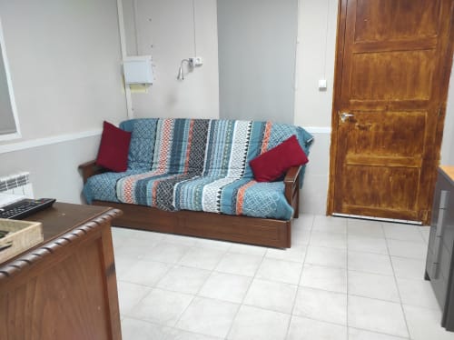 Acogedora sala de estar en Cuartel del Montsant con sofá de rayas azules, cojines rojos, muebles de madera y piso de baldosas.