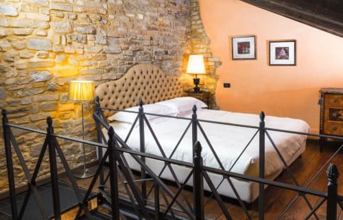 Bedroom in Le Calle Apartment at Dimora i Manichei, Monforte d'Alba with stone walls, black bed frame, upholstered headboard