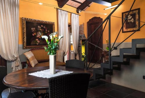 Elegant living room at Dimora i Manichei in Monforte d'Alba with orange walls, wooden dining table, and ornate artwork