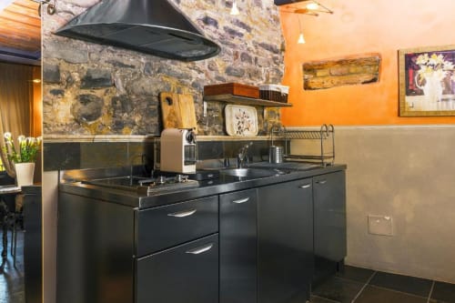 Modern kitchenette in Le Calle Apartment at Dimora i Manichei, Monforte d'Alba, with black cabinetry and stone walls