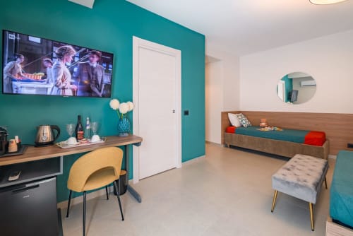 Camera moderna del Macramè Fazello con pareti turchesi, letto in legno, scrivania con sedia gialla, TV e vista sulla città di Sciacca