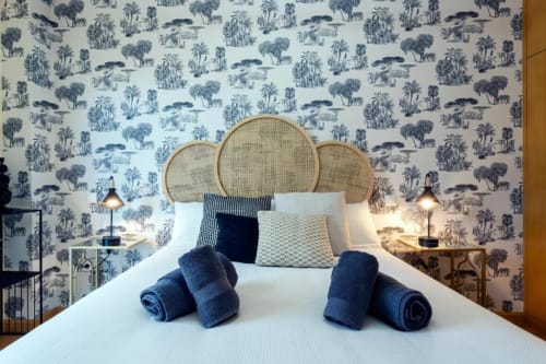 Elegante habitación en La Quinta Esencia de Burgos con cabecero de ratán, papel tapiz azul estampado, toallas enrolladas y lámpara colgante