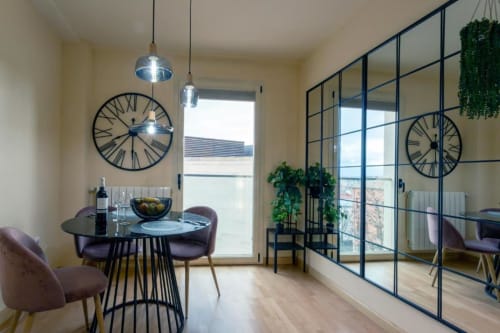 Comedor moderno en el apartamento La Quinta Esencia, Burgos, con mesa redonda, lámparas colgantes, relojes de pared y vistas a la ciudad