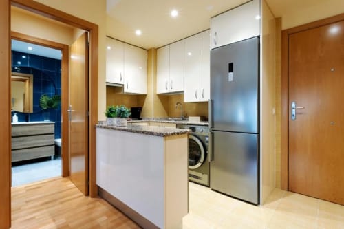 Cocina moderna en Burgos con electrodomésticos de acero inoxidable, muebles blancos, encimera de granito y suelo de madera