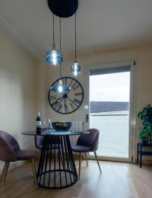 Comedor moderno en apartamento de Burgos con mesa redonda negra, lámparas colgantes y reloj grande en la pared
