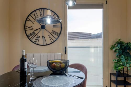 Comedor moderno en apartamento de Burgos con mesa redonda, botella de vino, reloj de pared y vistas al patrimonio por amplio ventanal