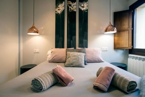 Dormitorio moderno en apartamento Arco San Esteban de Burgos con lámparas colgantes de cobre, toallas enrolladas y cuadros con vistas a la montaña