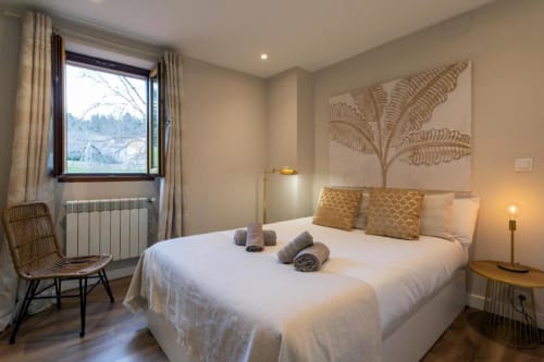 Dormitorio luminoso en apartamento de Burgos con cama blanca, arte botánico, vistas a montaña, suelo de madera y comodidades modernas