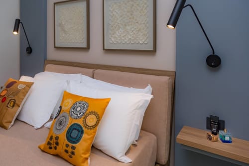 Camera Cricket Macramè Fazello a Sciacca con testiera beige, cuscini bianchi, pouf geometrico colorato, quadri e arredamento elegante