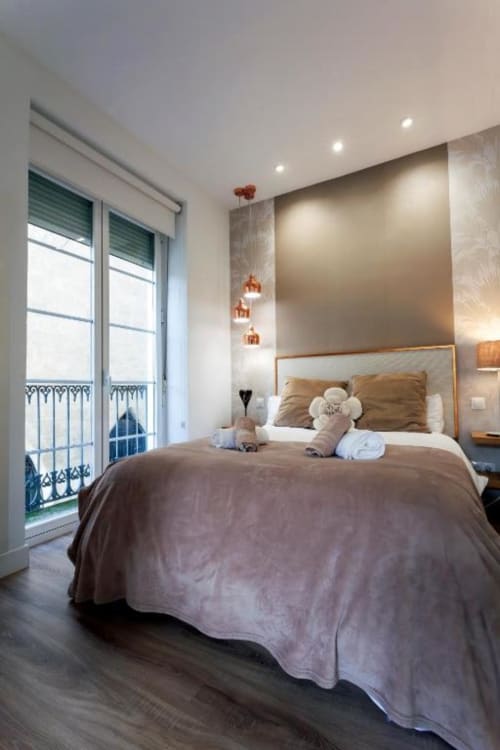Dormitorio moderno en apartamento de Burgos con vistas al balcón, pisos de madera, luces colgantes y acceso a la catedral