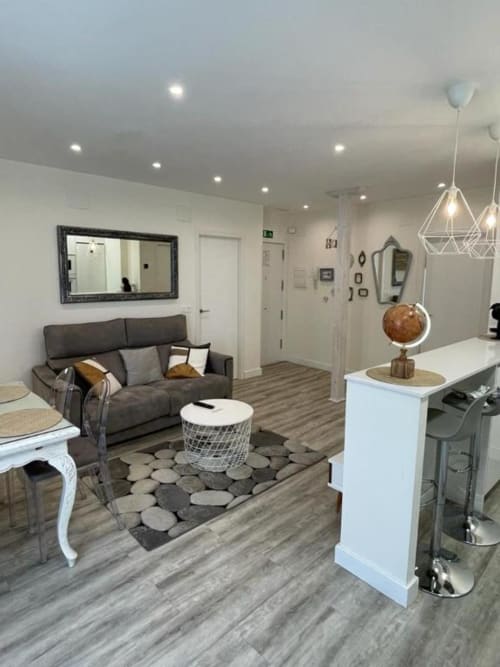 Sala moderna en apartamento Valeria's Corner en Burgos con sofá gris, cocina blanca, lámparas colgantes y piso de madera