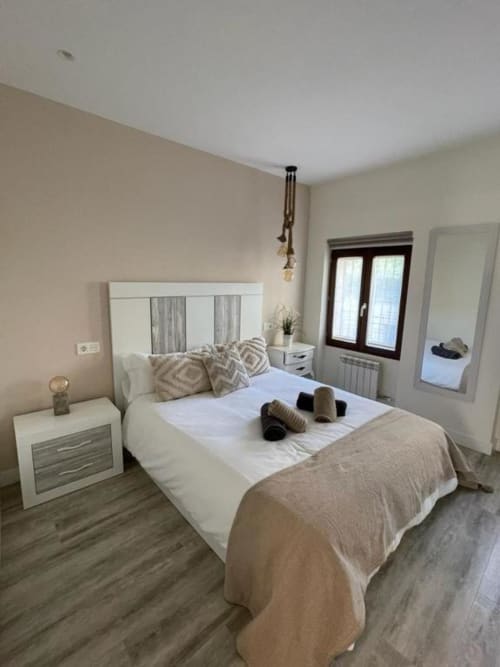 Dormitorio moderno en Valeria's Corner, Unique Rooms Burgos, con cama blanca, cabecero espejado y piso de madera