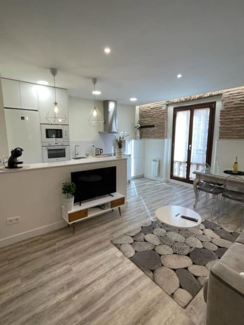Cocina abierta y sala de estar modernas en Burgos con muebles blancos, electrodomésticos de acero inoxidable y pantalla plana