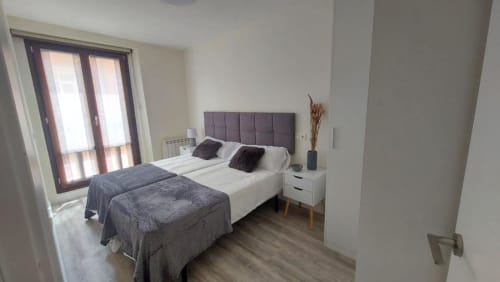 Dormitorio moderno en apartamento Valeria's Corner, Burgos con cabecero acolchado gris, ropa de cama blanca y puertas balconeras