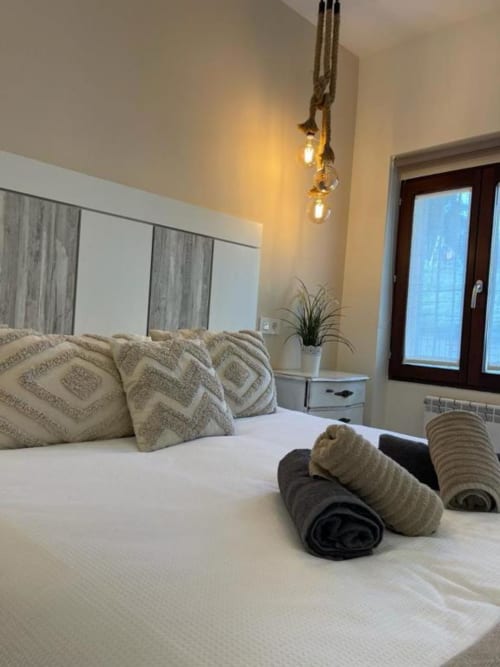 Dormitorio moderno en Valeria's Corner, Unique Rooms Burgos, con almohadas geométricas, toallas enrolladas, lámpara colgante y madera oscura