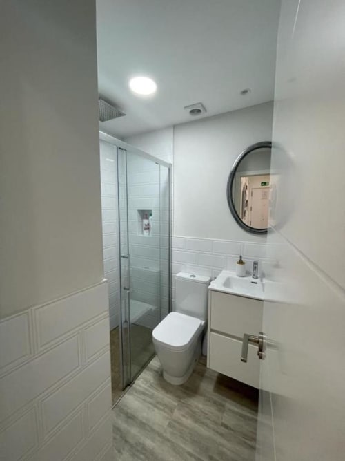Baño moderno en apartamento Valeria's Corner, Burgos. Con ducha a ras de suelo, tocador blanco, espejo redondo y diseño minimalista