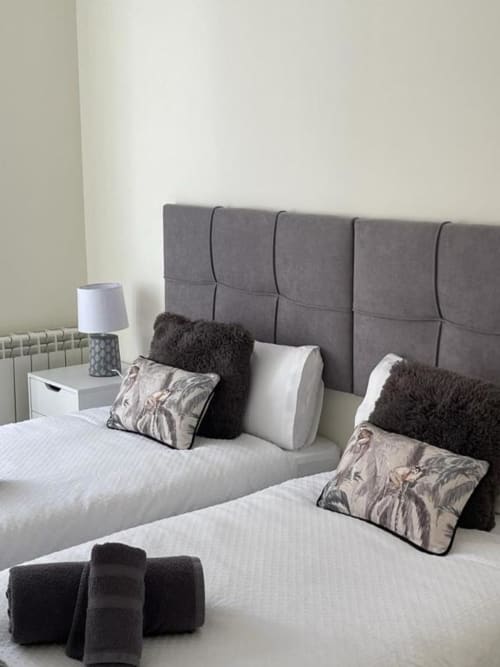 Habitación moderna en Valeria's Corner, Burgos con cabecero tapizado gris, ropa de cama blanca y cojines decorativos