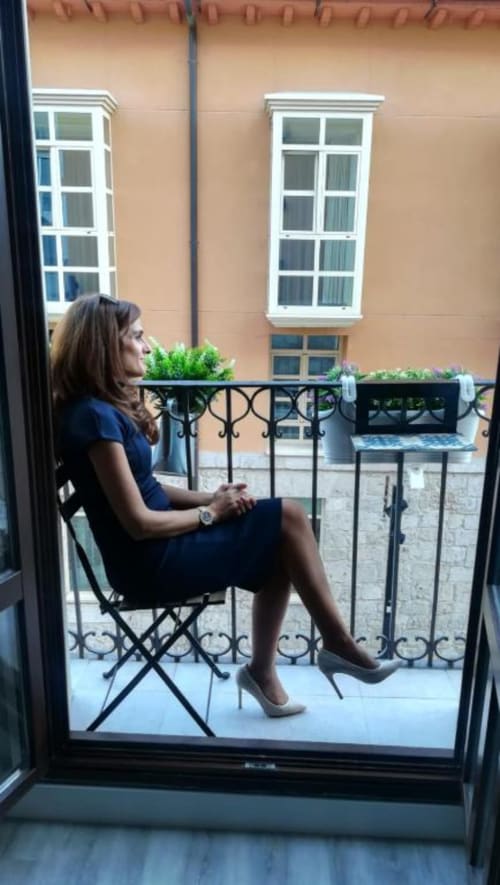 Mujer relajándose en silla de balcón en la esquina de Valeria en Burgos, frente a fachada de edificio color durazno