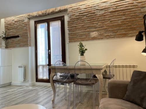 Sala de estar moderna en Burgos con vigas de madera vista, mesa de comedor, sillas transparentes y sofá crema en Unique