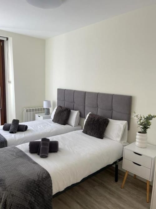 Habitación doble moderna en Valeria's Corner, Burgos, con cabecero tapizado gris, ropa de cama blanca, almohadas oscuras