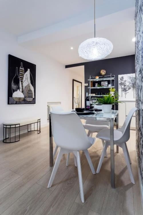 Comedor moderno en apartamento Spacio Menina, Burgos con sillas blancas, mesa de cristal, lámpara colgante y pared negra